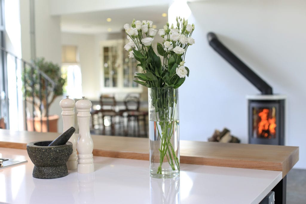 Deddington tall vase of white flowers in a sleek airy kitchen featuring a wood stove